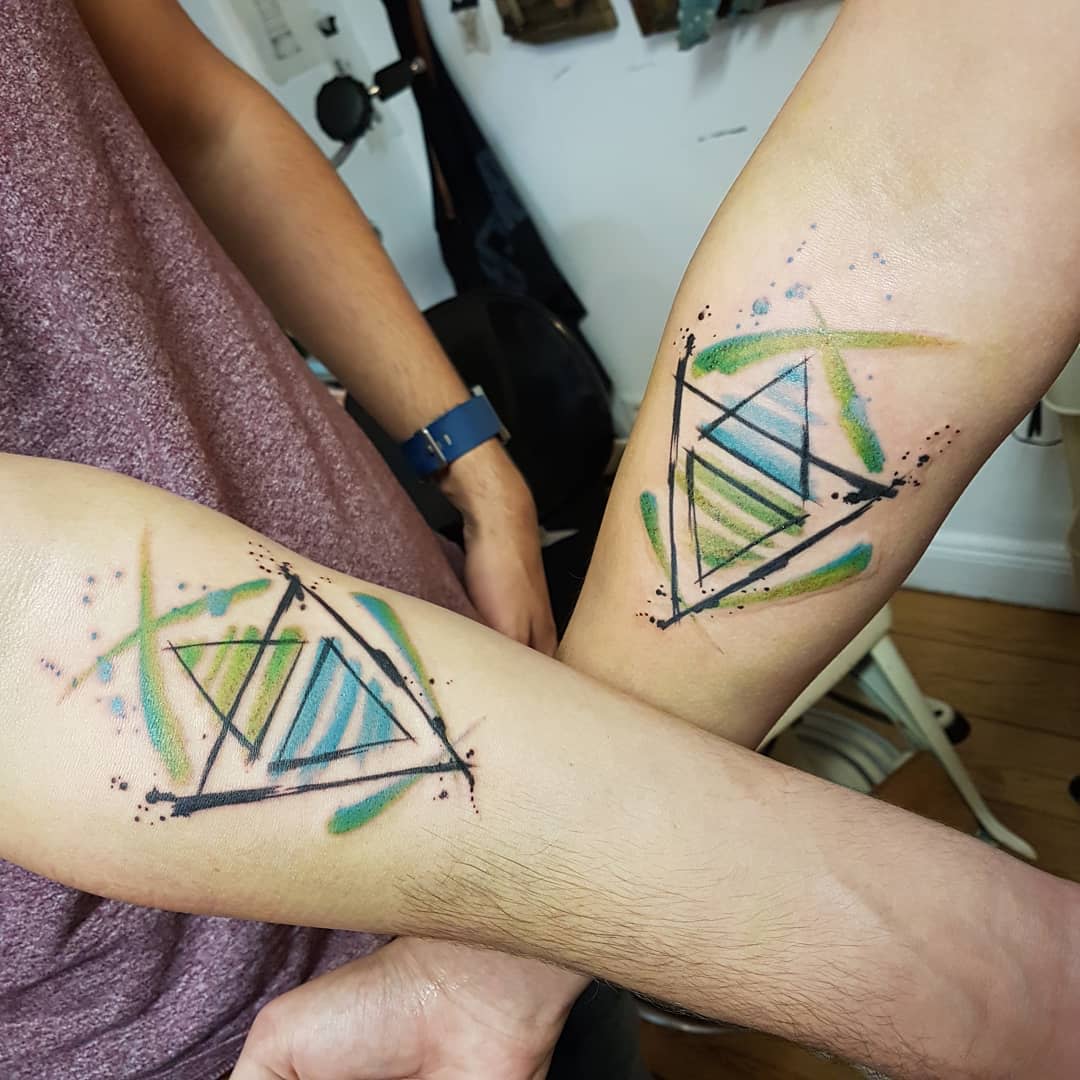 Matching abstract geometric tattoos with watercolor blue and green triangles, symbolizing a strong bond and connection